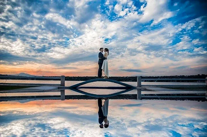 Novios en el muelle con el reflejo del cielo en el lago