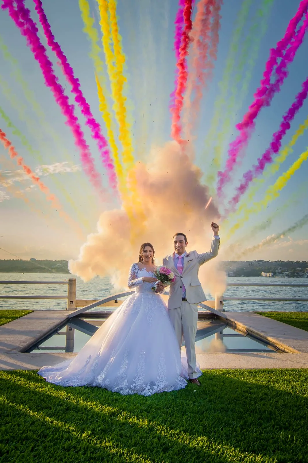 Novios frente al lago entre estelas de humo de colores al atardecer