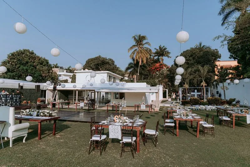 Jardín con mesas vestidas de blanco bajo los árboles junto al agua