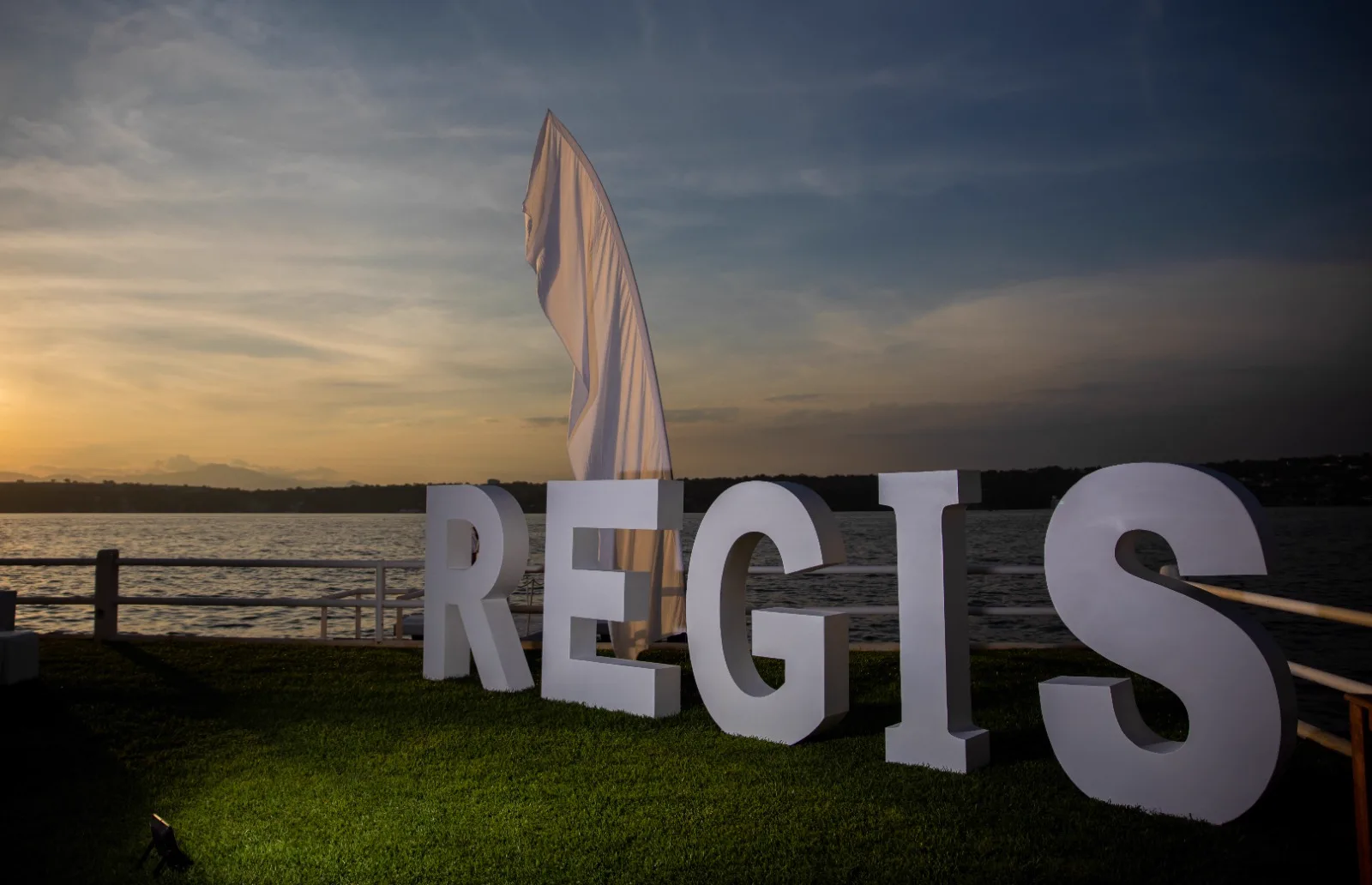 Letras decorativas sobre el césped frente al lago durante el atardecer